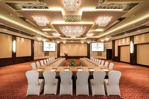 Una sala conferenze con un lungo tavolo, sedie bianche e pavimento rivestito di moquette.