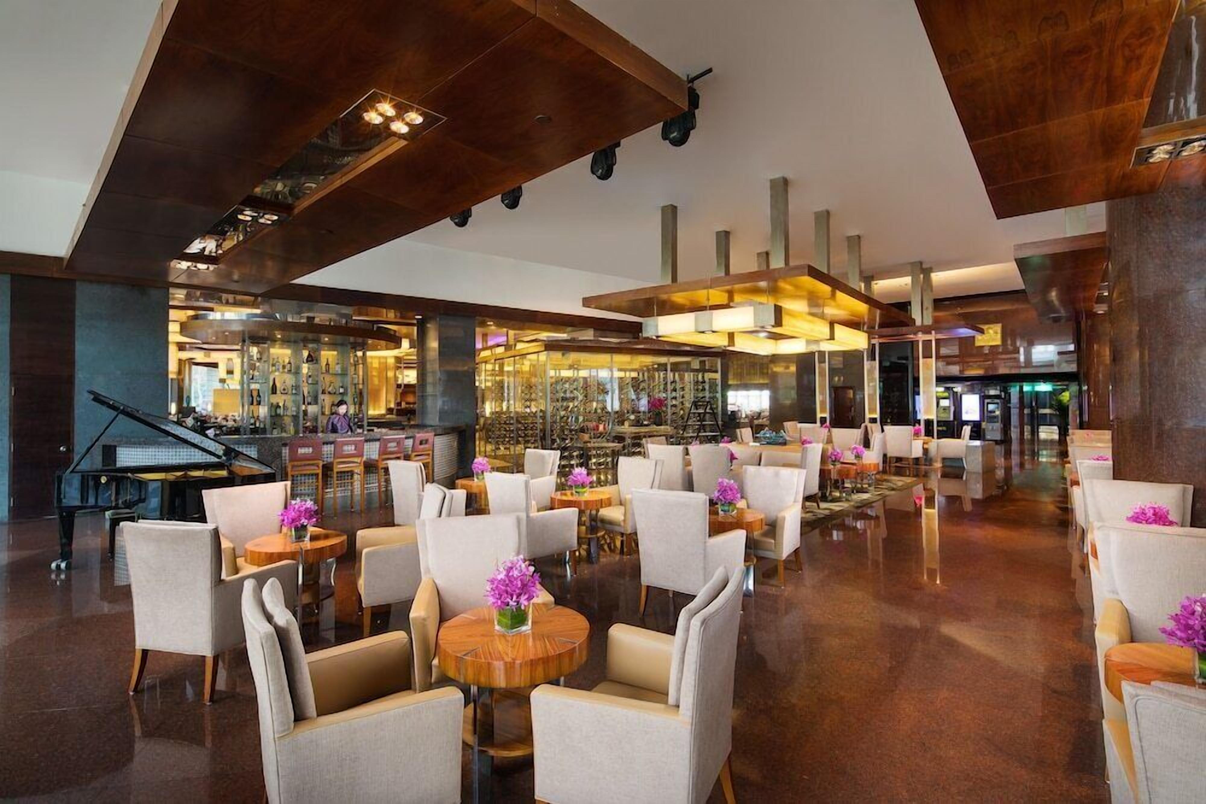 A spacious lobby with a grand piano, multiple seating areas, and a bar with a wine display.