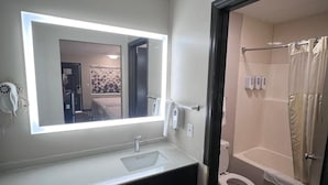 Ein modernes Badezimmer mit großem Spiegel, Waschbecken, Toilette und Duschbereich.