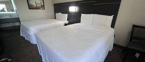 Una habitación de hotel con dos camas individuales, un cabecero oscuro, un escritorio pequeño y una silla.
