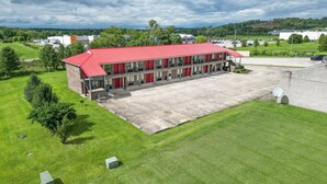 Ein Motel mit rotem Dach, mehreren Zimmern, einem Parkplatz und einem Rasen mit Bäumen.
