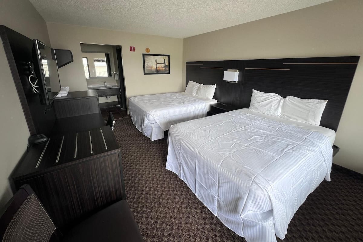 A hotel room with two beds, a desk, a chair, a television, and a bathroom.