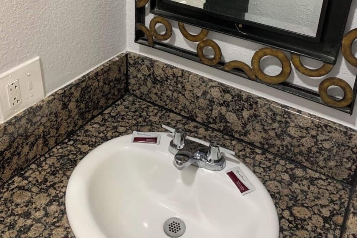 A bathroom with a white sink, granite countertop, and a mirror with a decorative frame.
