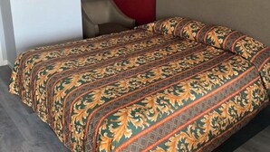 Un letto con copriletto decorato, una testiera e una sedia in una stanza con una parete rossa e pavimento in legno.