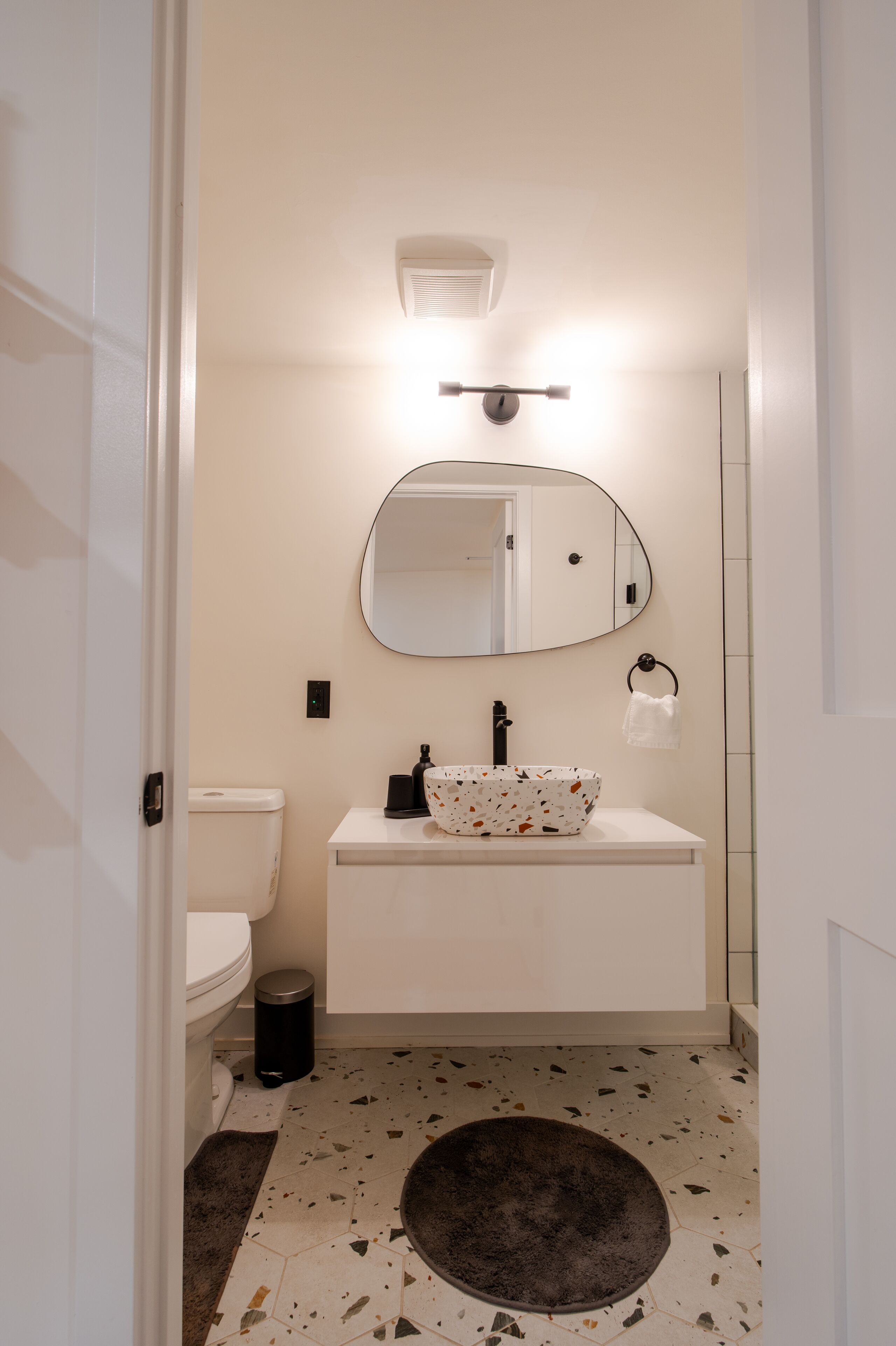 Une salle de bain équipée de toilettes, d’un lavabo, d’un miroir et d’un tapis rond posé sur le sol.