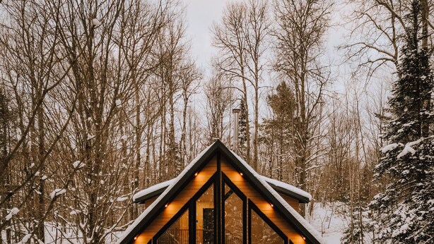 Une cabane dotée d’une grande façade vitrée, d’une terrasse en bois et d’un espace extérieur aménagé et abrité.