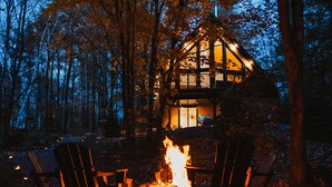 Une cabane avec un foyer au centre, entourée de chaises et d’arbres.
