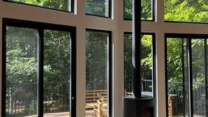 Une pièce spacieuse avec de grandes fenêtres, une cheminée et une vue sur une terrasse et des arbres.