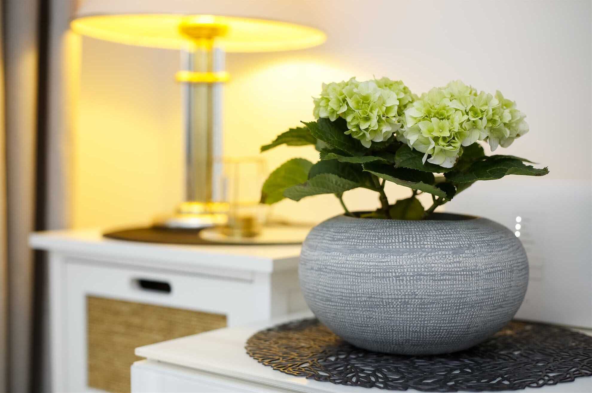 A grey textured vase with green hydrangea flowers on a white bedside table.
