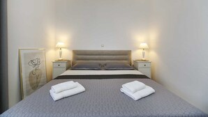 Een net opgemaakt bed met twee kussens, een nachtkastje met een lamp, en een lijstje met een afbeelding aan de muur.