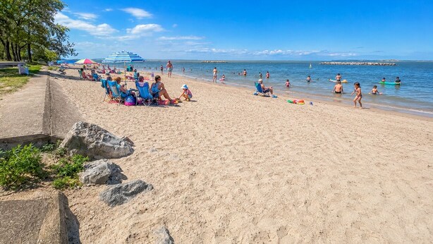 Ein Strand mit Menschen, die auf Stühlen entspannen und sich sonnen, einem klaren blauen Himmel und ruhiger See.