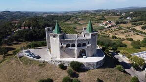 Un château doté de deux flèches vertes, entouré de douves et comprenant un parking où sont stationnées plusieurs voitures.