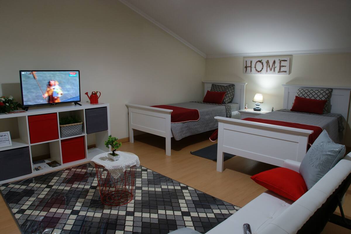 A modern bedroom with a TV, two beds, a white wardrobe, and a 'HOME' sign on the wall.