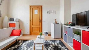 Un espace de vie compact comprenant un canapé, une petite table, un téléviseur et un meuble agrémenté de plantes.