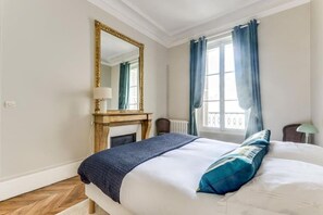 A hotel room with a bed, a mirror, a fireplace, and a window with curtains.