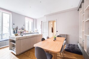 A modern kitchen with a central island, a dining table with chairs, and a view of the city through large windows.
