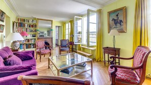 Un salon spacieux avec une cheminée, une bibliothèque et une grande fenêtre ornée de rideaux jaunes.