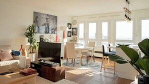 Ein modernes Wohnzimmer mit Flachbildfernseher, einer Couch, einem Esstisch mit Stühlen und einem großen Fenster mit Blick auf die Stadt.