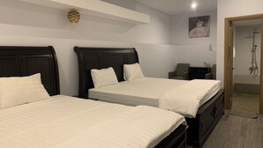 Hotellihuone, jossa on kaksi sänkyä, tuoli, työpöytä ja suihkutila.