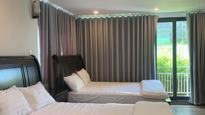 Hotellihuone, jossa on kaksi sänkyä, tumma pääty ja ikkunasta avautuva näkymä vehreään maisemaan.