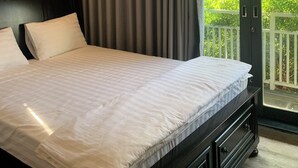 Hotellihuone, jossa on suuri sänky, tumma pääty ja näkymä vehreään maisemaan liukuovien takaa.