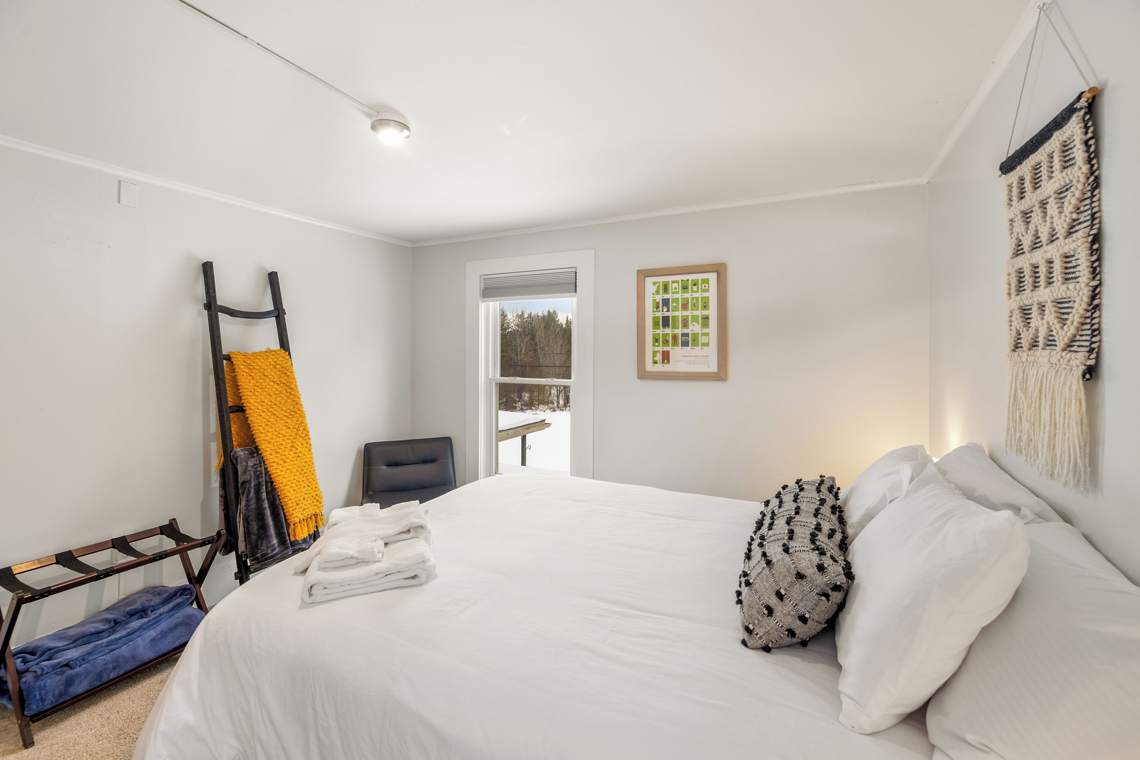 Une chambre d’hôtel avec un grand lit, une chaise, un banc, une fenêtre et une décoration murale en macramé.