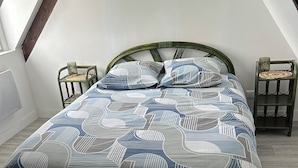 A bedroom with a bed, a chair, a nightstand, and a window.