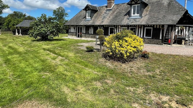 A traditional half-timbered house with a well-maintained lawn and a yellow flowering bush in the foreground.