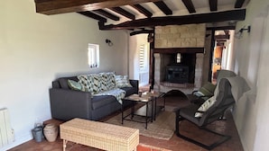 A cozy living area with a sofa, armchair, and a small table. There's a stone fireplace and a tiled floor.