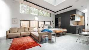 A modern living room with a sofa, a bed, a dining table, and a kitchen area.