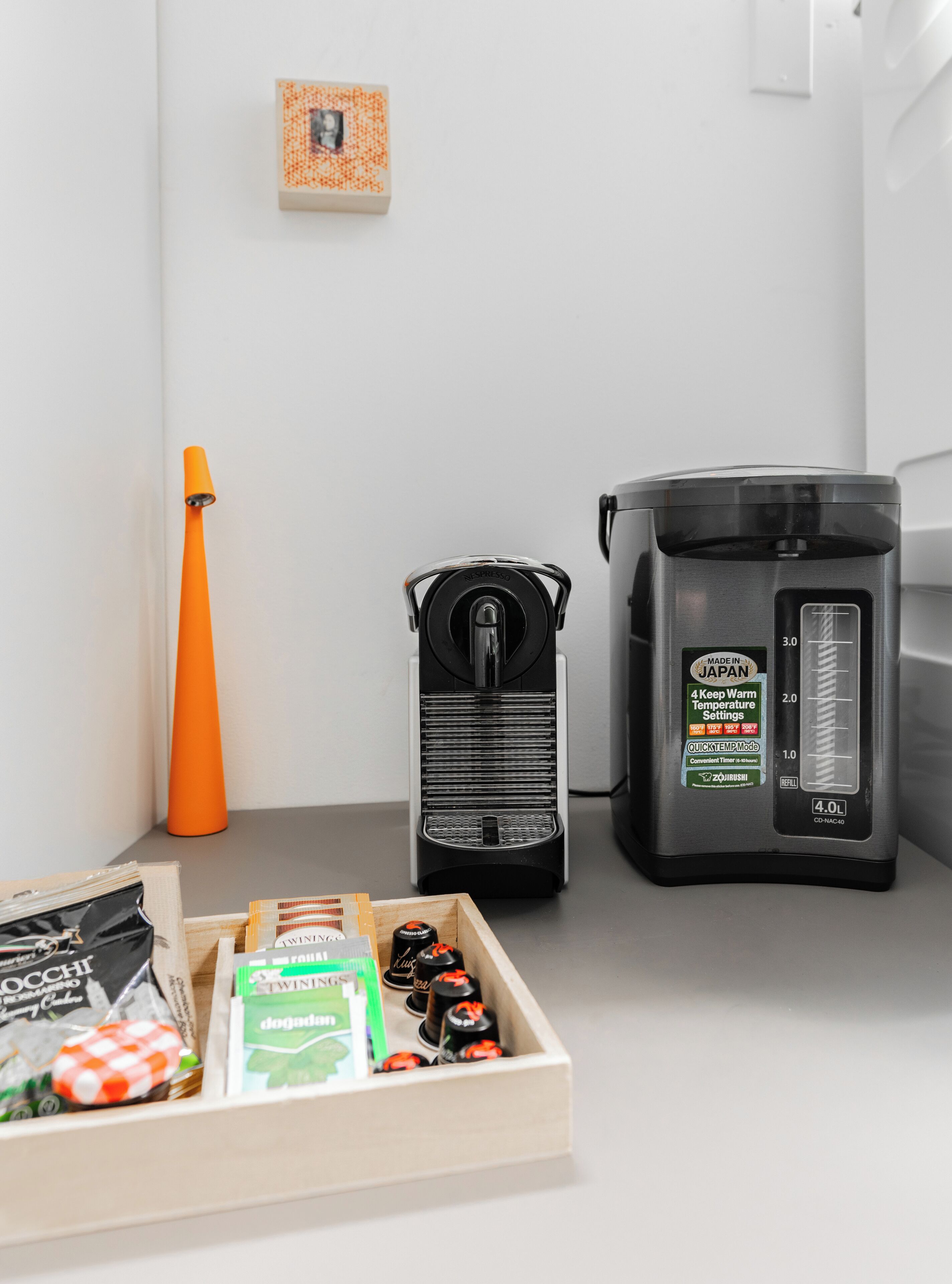 Una kitchenette con cafetera, dispensador de agua y un recipiente para cápsulas de café.