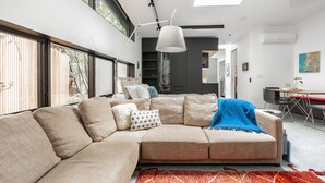 A modern living room with a large L-shaped sectional sofa, a dining area with a table and chairs, and a kitchen in the background.