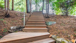 A wooden staircase leading up a hill, surrounded by trees and a stone wall.