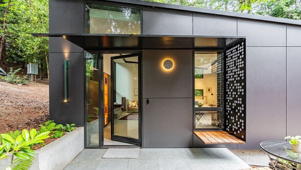 A modern house with a glass door entrance, a wooden deck, and a garden area.
