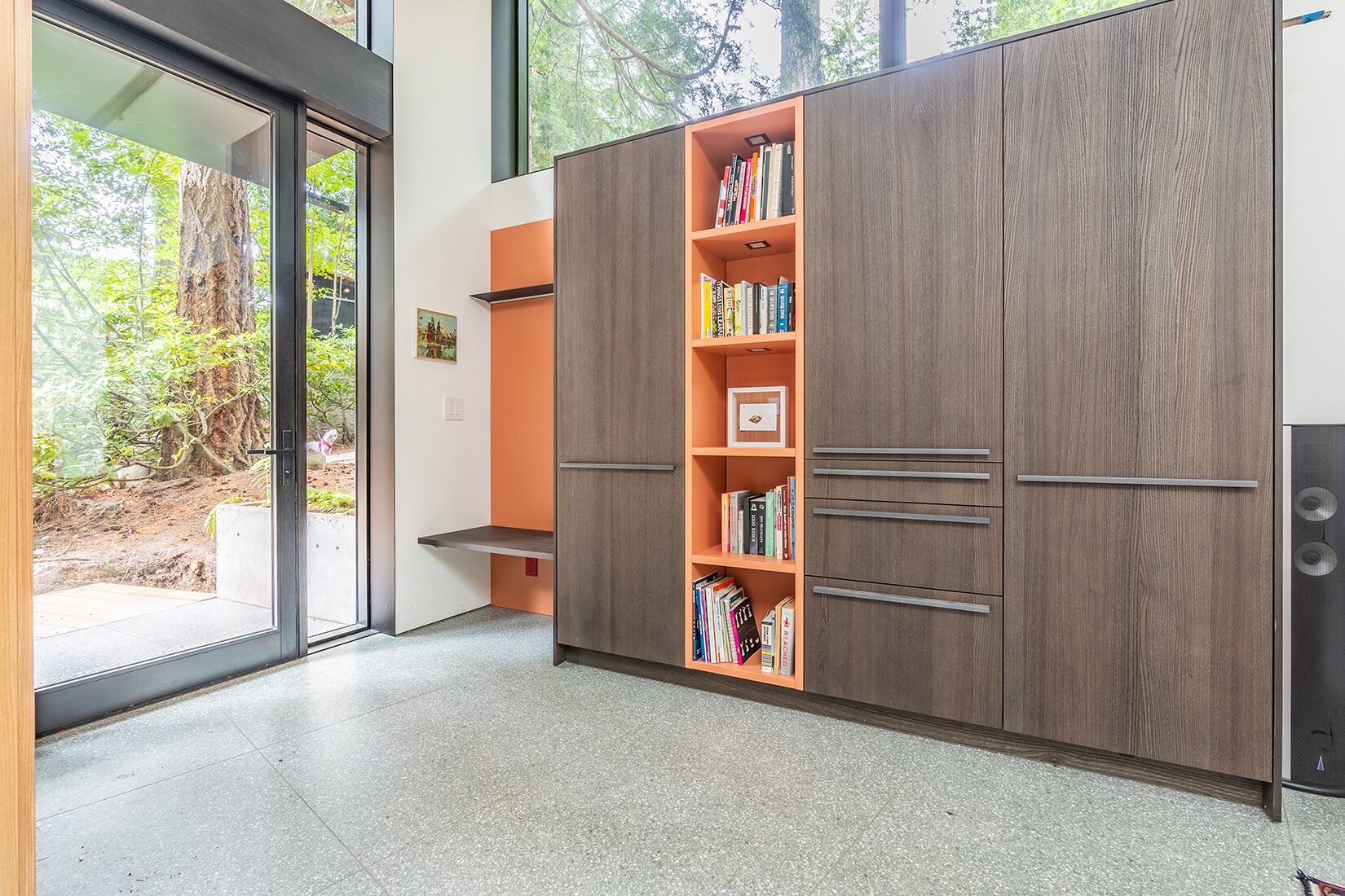 A modern room with a large wardrobe, a bookshelf, and a sliding glass door leading to a garden.