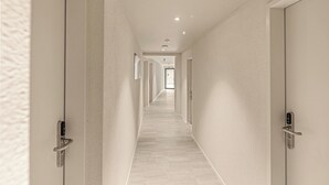 Un pasillo moderno con piso y paredes de tonos claros, que conduce a una puerta al final.