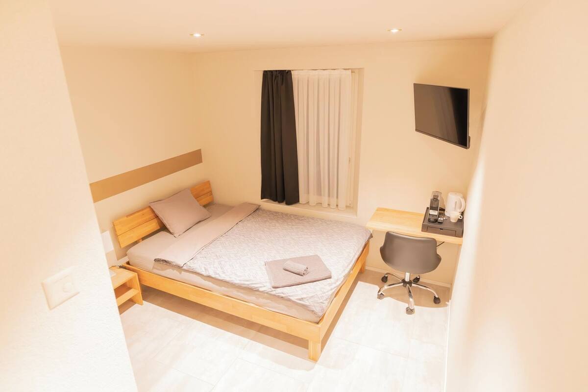 A bedroom with a bed, bedside table, chair, and a TV mounted on the wall.