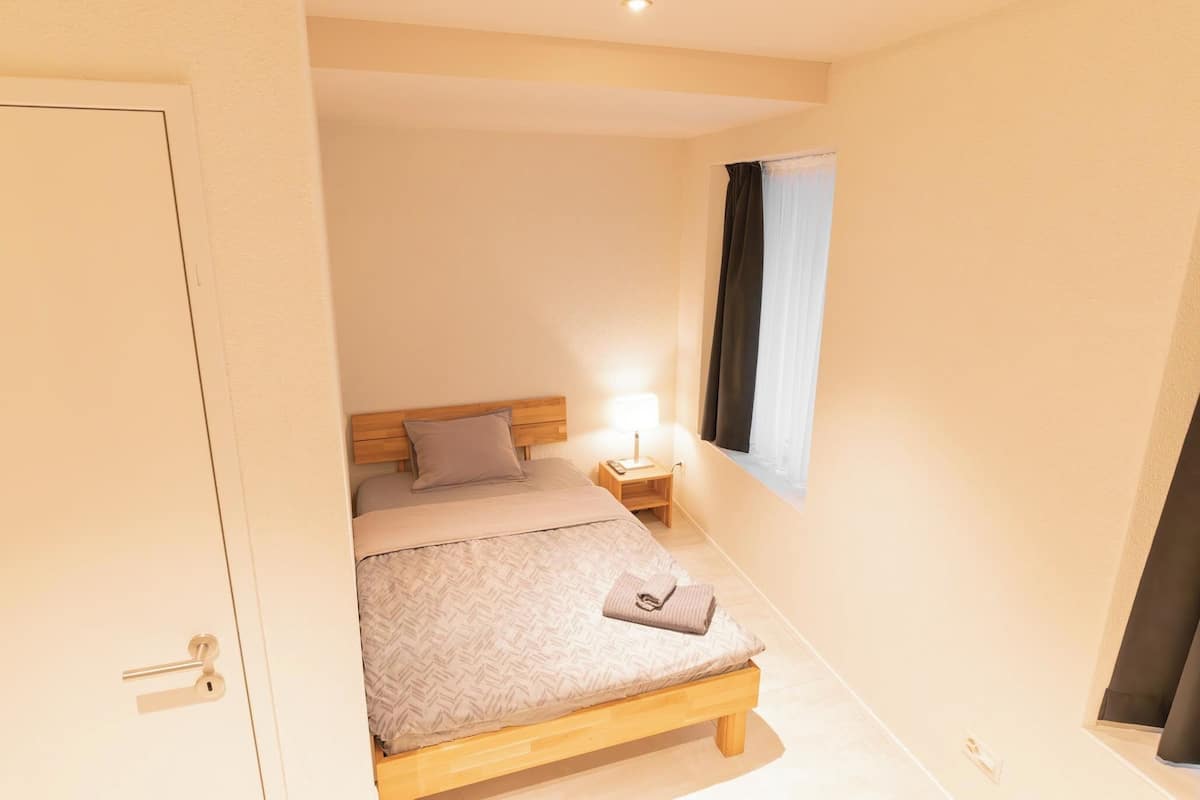 A bedroom with a bed, bedside table, lamp, and window.