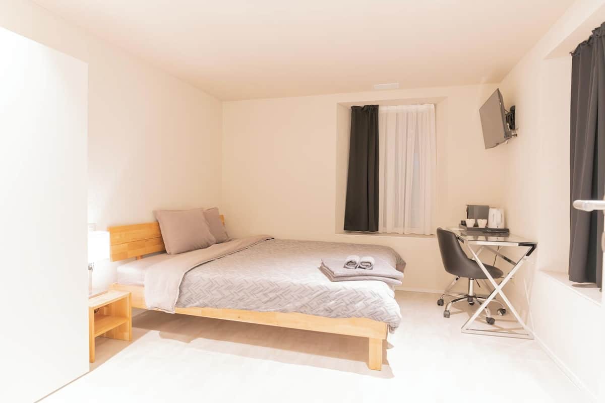 A small, modern bedroom with a bed, bedside table, and a desk with a chair.