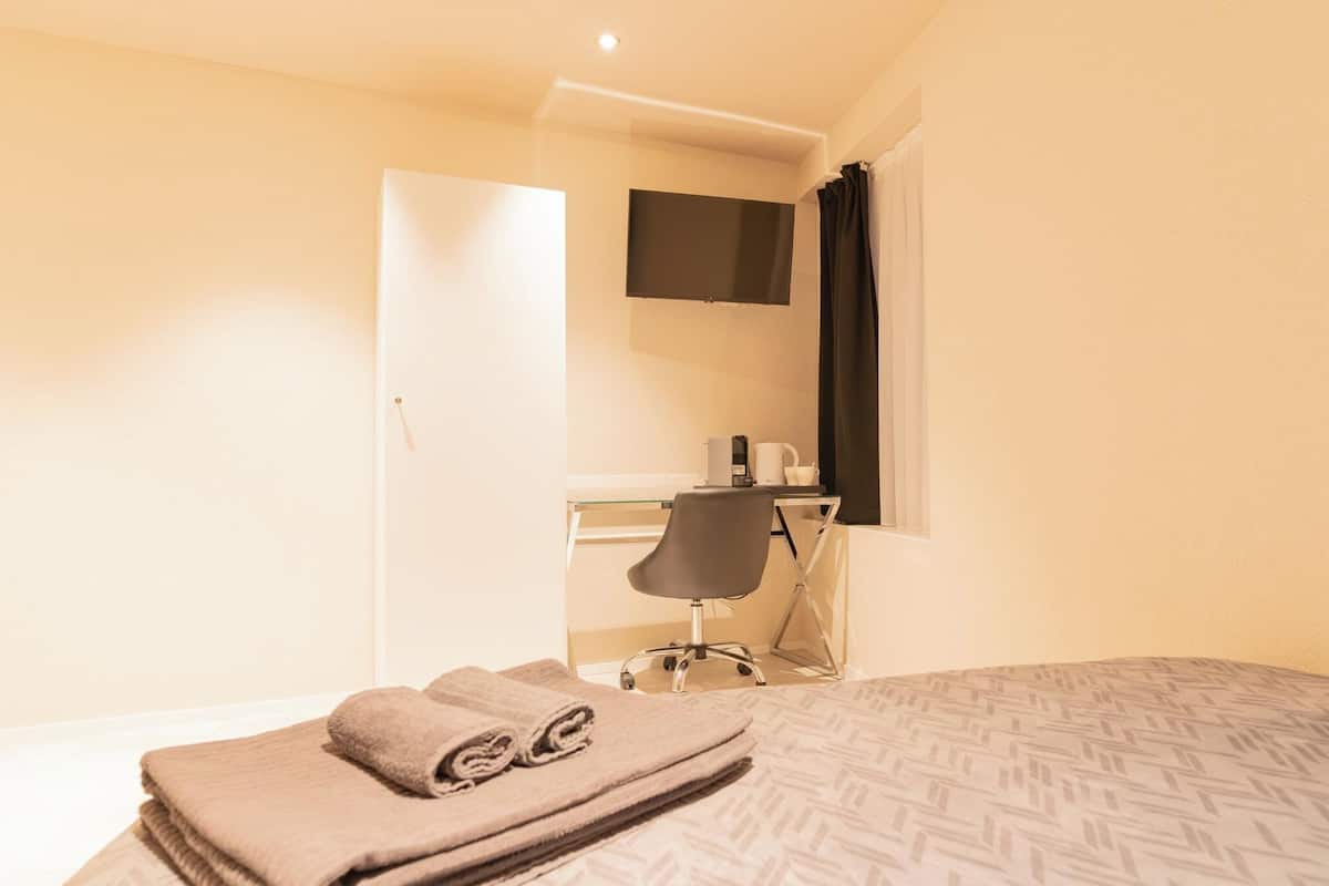 A hotel room with a bed, a desk with a chair, a flat-screen TV, and a window with curtains.