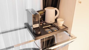 Un minibár de hotel con una cafetera, un molinillo de café Krups, un dispensador de cápsulas de café y una taza.