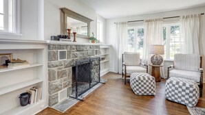A living room with a stone fireplace, white walls, wooden flooring, and a checkered ottoman. - Spacious 5bdrm house with AC and WiFi /Family Friendly/Fire Pit /HOT TUB (Gordonville)