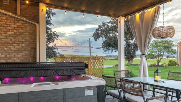 A patio area with a hot tub, outdoor seating, and a view of the countryside. - Spacious 5bdrm house with AC and WiFi /Family Friendly/Fire Pit /HOT TUB (Gordonville)