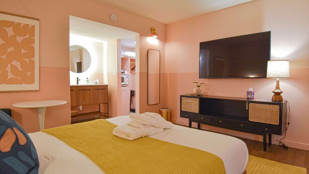 Una habitación de hotel con una cama, televisión, espejo, cómoda y una pequeña mesa.