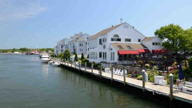 Un hotel frente al agua con una hilera de edificios blancos, un muelle y un cielo azul despejado.