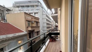 Un balcone stretto con pavimento in legno, ringhiera in metallo e vista sugli edifici vicini.