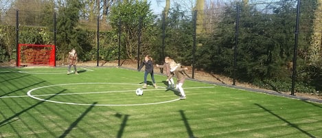 Een buitenvoetbalveld met een doelpaal, omringd door bomen en een hek.