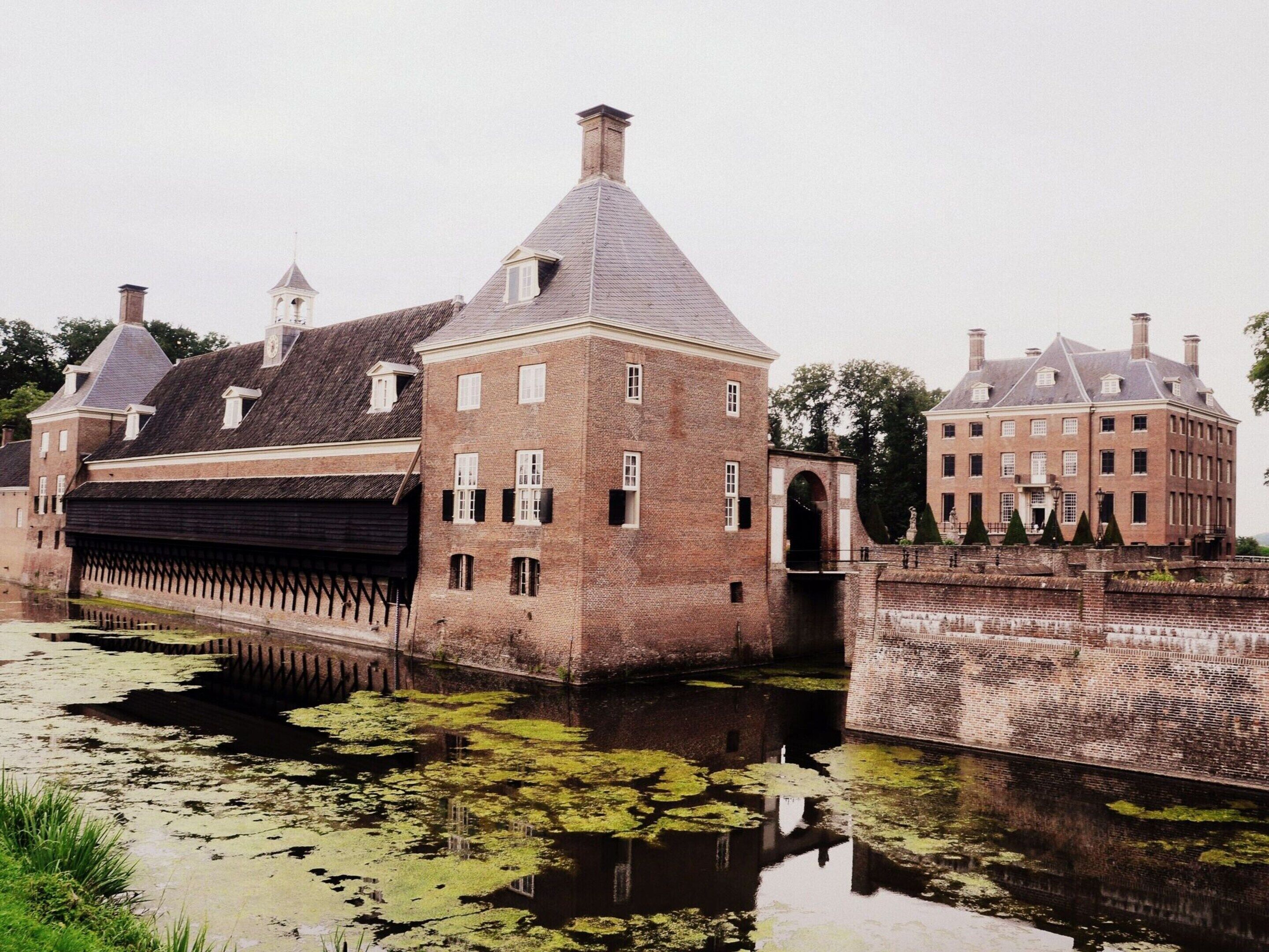 A historic building with a canal in front, featuring a bridge and a reflection in the water.