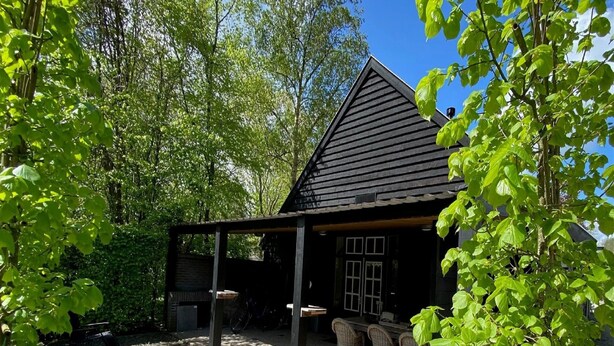 A rustic wooden cabin with a covered porch, a gravel patio, and wicker furniture. - Apartment in Wageningen Near Rhine River (Elst)