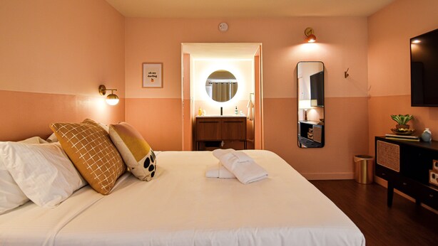 A hotel room with a large bed, a bedside table, a mirror, a small cabinet, and a television. - Mid-Century Themed Hotel Room in Fayetteville, AR - The Clementine on College #5 (Fayetteville)